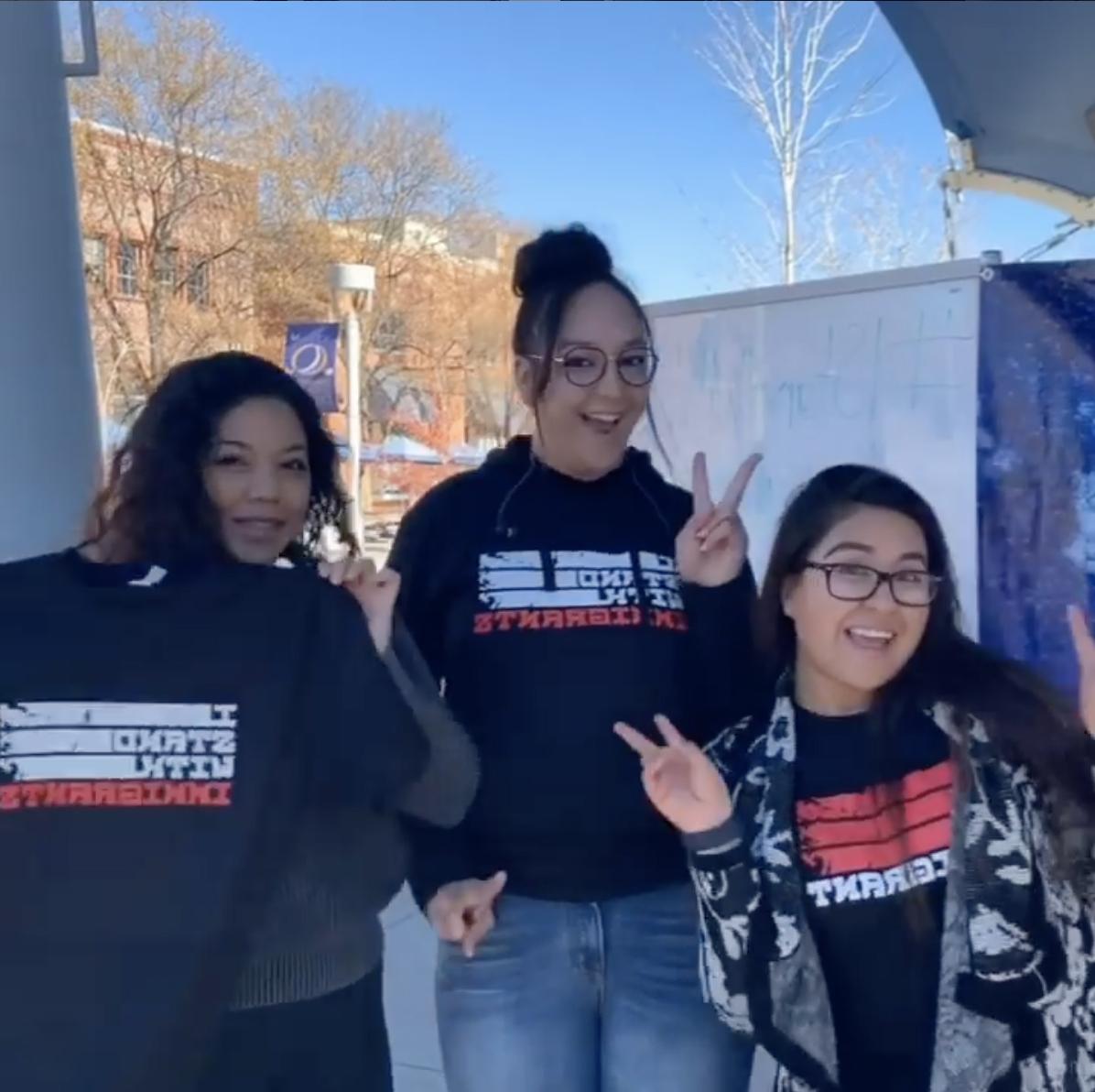 Three females holding or wearing shirts that say 